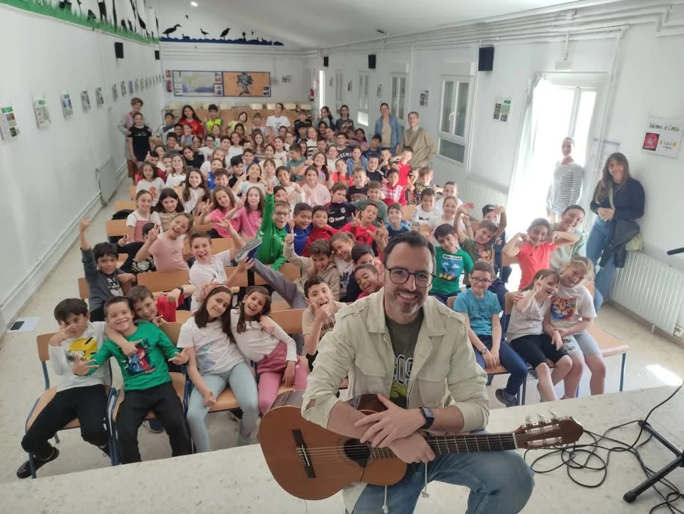 César con la guitarra y un grupo de alumnos y alumnas en un encuentro escolar.