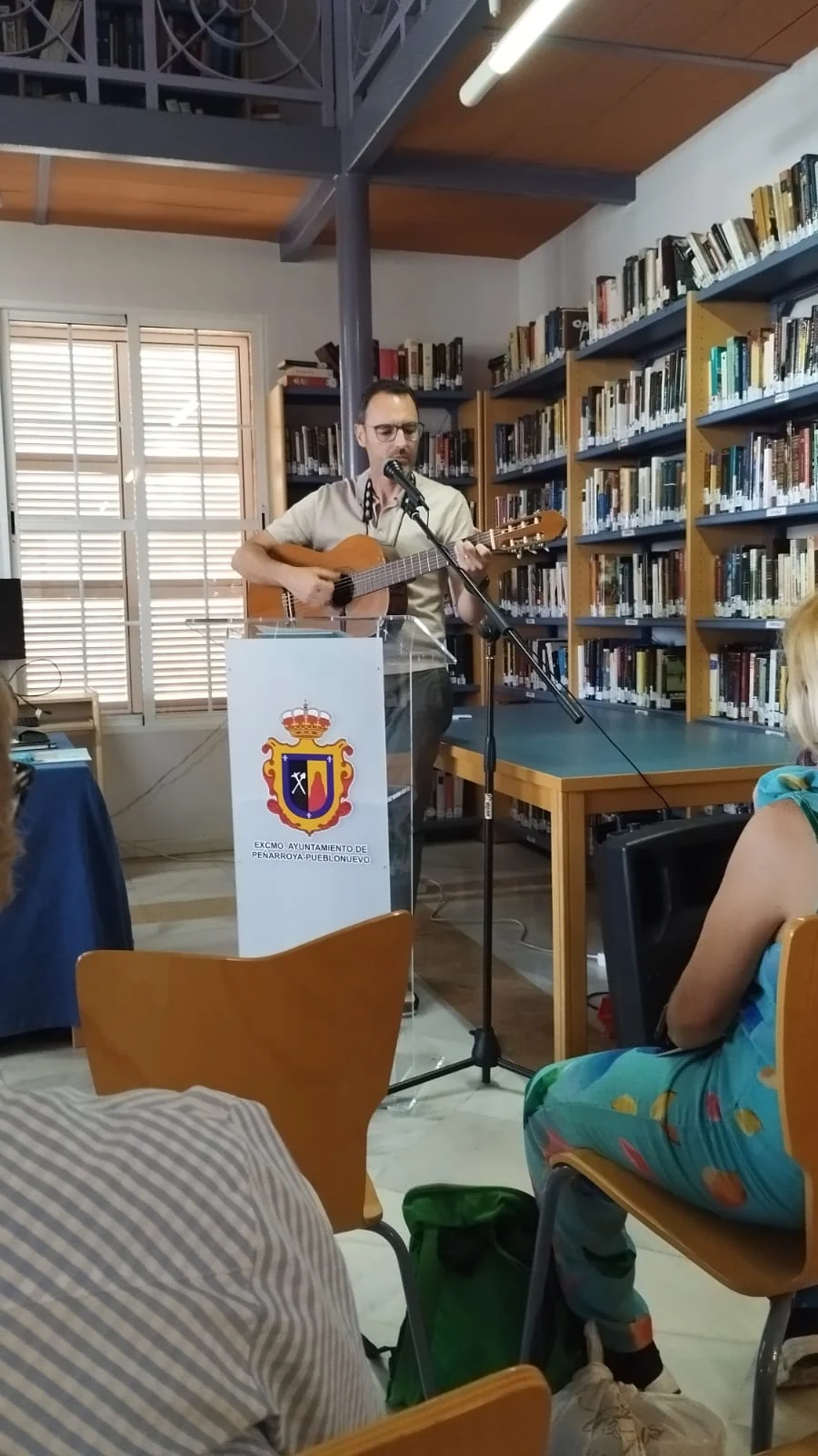 César comparte una lectura desde un atril en una biblioteca.