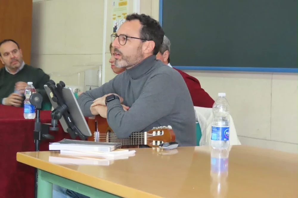 César conversa con el público, sentado junto a su guitarra en una mesa.